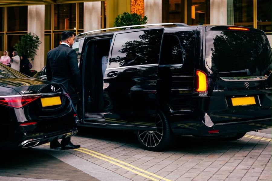 Heylux chauffeur holding the door of a Mercedes V-Class beside an S-Class at a London hotel