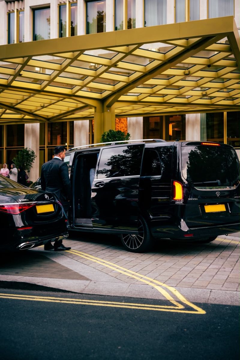 Heylux chauffeur holding a Mercedes V-Class door open at a London hotel