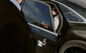 Passenger seated in the back of a chauffeur-driven car with the door held open