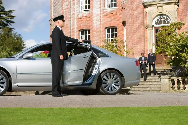 Chauffeur standing beside a luxury car outside a Cotswolds country estate