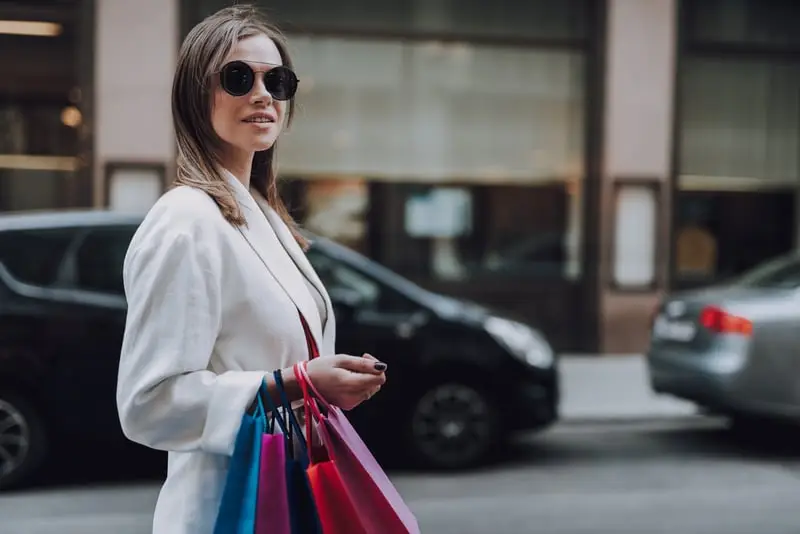 Shopper carrying luxury shopping bags beside a waiting car on a Knightsbridge and Chelsea shopping trip